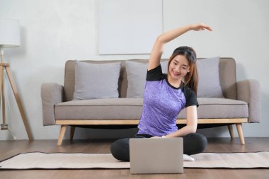 Genç Asyalı kadın dizüstü bilgisayarda spor videosu izliyor ve egzersiz sonrası rahatlamak için kolunu uzatıyordu..