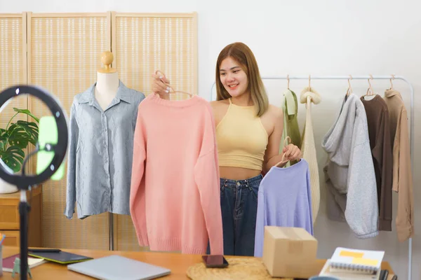 Online merchant concept, Fashion designer showing clothes for sale in live streaming at home office.