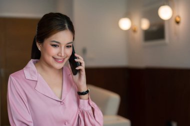 Kadın girişimci, müşterisiyle akıllı telefondan konuşuyor ve dahili ofiste yeni bir başlangıç hakkında çalışıyor..