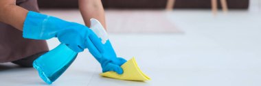 Hizmetçi eldiven giyiyor ve yere toz silmek için daha temiz sprey ve mikrofiber bez kullanıyor..