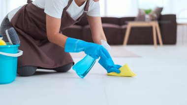 Hizmetçi eldiven giyiyor ve yere toz silmek için daha temiz sprey ve mikrofiber bez kullanıyor..