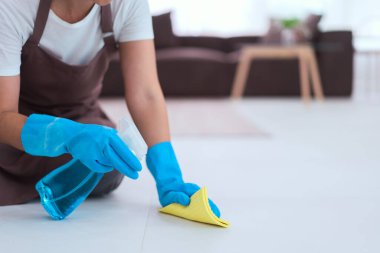 Hizmetçi eldiven giyiyor ve yere toz silmek için daha temiz sprey ve mikrofiber bez kullanıyor..