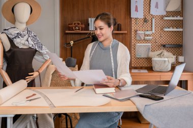Moda koleksiyonu tasarlamaya çalışan Asyalı terzi kadınlar ve belge üzerindeki elbise çizimlerini kontrol ediyorlar.