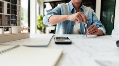 Kadın mühendis geometri pusulası kullanır ve ofisteki planlar üzerine inşaat çizimi için çalışır.