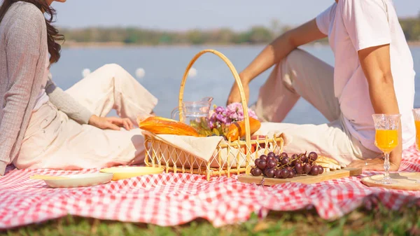 Young couple in love sitting on blanket with breakfast basket of bread and fruit to picnic together.