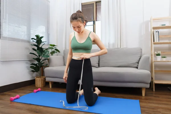Healthy and weight loss concept, Young Asian woman is measuring her waist with tape measure.