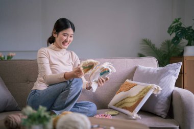 Genç Asyalı kadın, hobi olarak işlemeli kumaş çerçeve ve yumruk iğnesi tekniğine bakıyor..