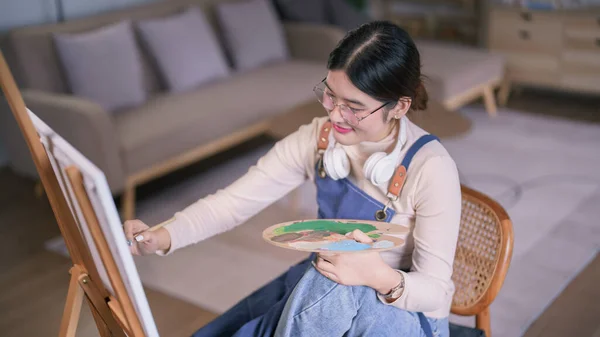 Genç Asyalı Kadın Sanatçı Boynuna Kulaklık Takıyor Tuvale Boya Fırçası - Stok İmaj