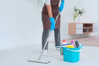 Temizlikçi, oturma odasının yerlerini temizlemek için plastik temizlik malzemesiyle paspas kullanıyor..