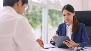 Avukat kadın iş adamına iş sözleşmesi hakkında danışmanlık yaparken tablete veri yazıyor..