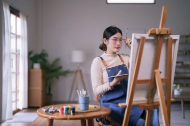 Genç Asyalı kadın sanatçı gözlüklere dokunuyor ve düşünce tablosu çiziyor..