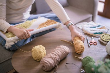 Asyalı bir kadın, hobi olarak kumaş üzerine işleme yaptıktan sonra masaya iplik koyuyor..