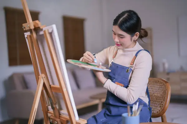 Young asian female artist squeeze color out of tube on color palette for painting artwork on canvas.