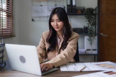 Dişi mimar, dizüstü bilgisayardaki inşaat planını ve bina projesinin planını incelemek için çalışıyor..