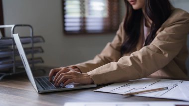 Dizüstü bilgisayarında mimari plan yazmaya çalışan kadın mimar inşaat projesinin planıyla birlikte..