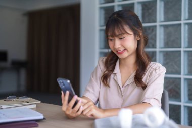 Gündelik giysiler içinde Asyalı genç bir öğrenci, öğretim görevlisi eğitimi alırken ve öğretim görevlilerini online olarak akıllı telefon dijital teknolojisiyle okuturken aynı zamanda bilgi verilerini okuyor ve üniversitede ödev yapıyor..