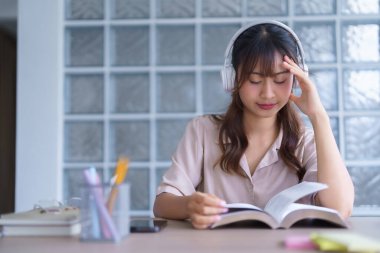 Gündelik giysiler içinde, kulaklık takmış, müzik dinliyor ve fikir üretmek için ders kitabı okuyor, aynı zamanda eğitim bilgisi okuyor ve üniversitede ödev yapıyor..