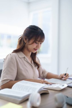 Eğitim bilgisi öğrendikten ve üniversite sınavına hazırlandıktan sonra hesap makinesi kullanarak ev ödevleri ve not defterine notlar yazan Asyalı genç bir öğrenci..