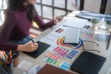 Grafik tasarımcısı serbest kadınlar yaratıcı fikirleri düşünerek ve logo markası çizmek için dijital tablet kullanarak ev stüdyosunda teknolojik ekipmanlarla grafik tasarımı hakkında çalışırken.