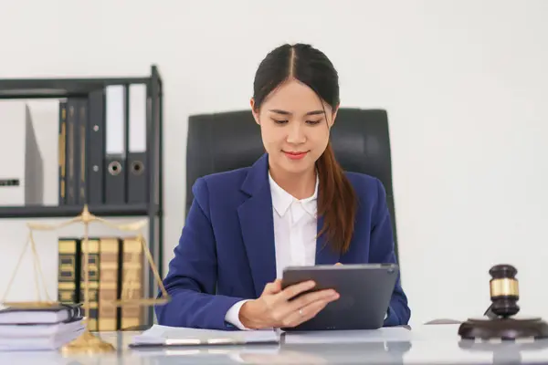 Lawyer woman working and writing data on tablet while reading business contract and legal agreement.