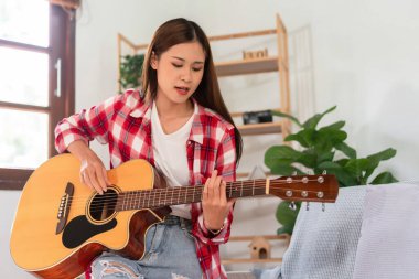 Hobby concept, Young asian woman learning and practice playing chords with acoustic guitar on couch.