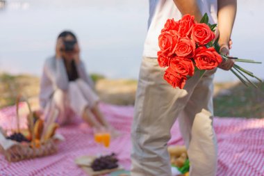 Arkasında gül buketi tutan genç bir adam ve kamerada fotoğraf çekmek için kız arkadaşına poz veriyor..