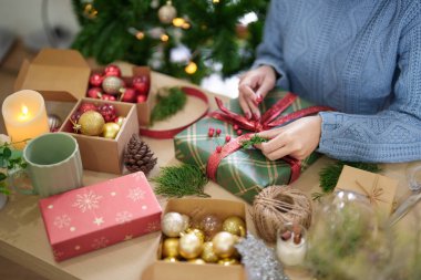 Mutlu kazaklı genç Asyalı kadın Noel hediyesini çam dalı ve kırmızı böğürtlenlerle süslerken Noel bayramı ve kış mevsimlerini kutlamak için hediyeler hazırlıyor..