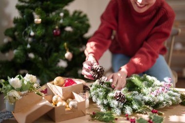 Noel çelengi üzerinde çam kozalağı ve kırmızı böğürtlen süsleyerek Noel bayramı ve kış mevsimlerini kutlamak için süsleri hazırlayan Asyalı genç bir kadın..