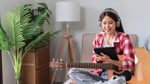 Guitar and singer concept, Young woman wear earphone and sit on couch to learning music on tablet.