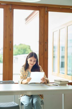 Eğitim ve okur yazarlık kavramı, üniversiteli kız üniversite kütüphanesinde ders kağıdı okuyor..
