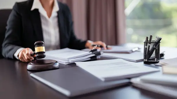 Lawyer businesswoman holding hammer in law firm while reading lawsuit and checking about financial business document to analysis about legislation agreement with terms data of business contract.