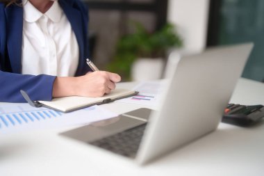 Pazarlama işi raporunu okuyan Asyalı iş kadınları, ofis dışındaki yatırım ve pazar stoklarını analiz ederken dizüstü bilgisayarda mali tabloları kontrol etmeye ve not almaya başladılar..