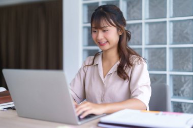 Üniversitede bilgi verileri yazarken ve dizüstü bilgisayar dijital teknolojisiyle çalışırken günlük giysiler içinde Asyalı genç bir öğrenci özel ders izliyor ve çevrimiçi öğretmenlik eğitimi alıyor..