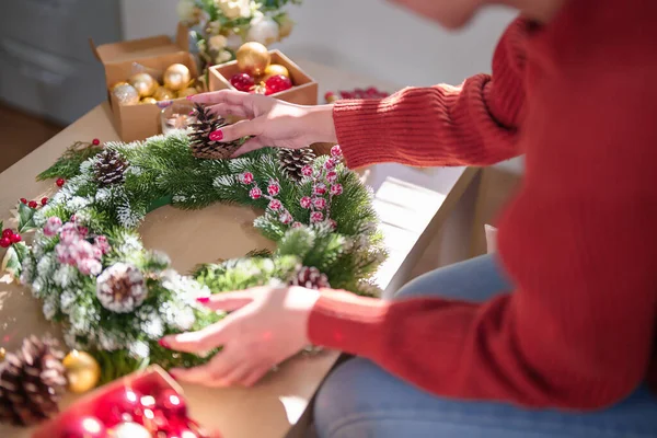 Noel çelengi üzerinde çam kozalağı ve kırmızı böğürtlen süsleyerek Noel bayramı ve kış mevsimlerini kutlamak için süsleri hazırlayan Asyalı genç bir kadın..