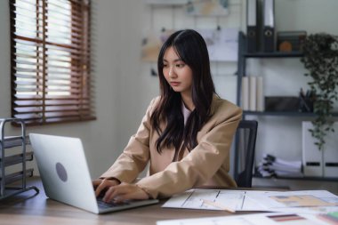 Dişi mimar, dizüstü bilgisayardaki inşaat planını ve bina projesinin planını incelemek için çalışıyor..