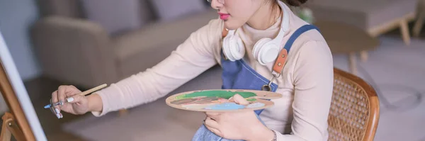Młoda Azjatycka Artystka Nosi Słuchawki Szyi Maluje Pędzlem Płótnie — Zdjęcie stockowe