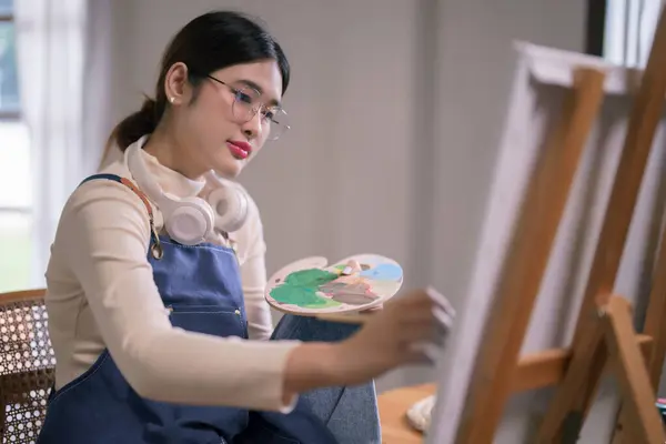 Young asian female artist use paintbrush and color to drawing and painting create artwork on canvas.
