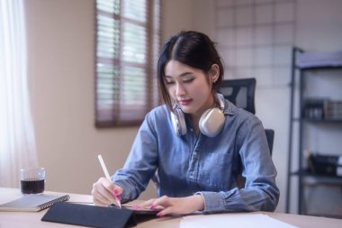 Genç Asyalı kadın öğrenciler ders çalışırken ve izlerken çevrimiçi derste dijital tablet üzerine notlar yazarken ev ödevlerini yaparken ve evden bilgi uzaktan eğitimi alırken öğreniyorlar..