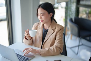 İş kadınları kahve içerken ve yeni başlatılan proje hakkında strateji ve yönetimi analiz etmek için çalışırken, iş yerlerindeki dijital dizüstü bilgisayarda yatırım ve iş dünyasının finansmanı hakkında rapor yazıyorlar..