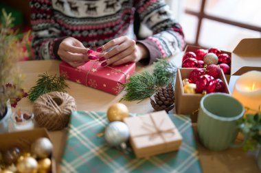 Genç Asyalı kadın, Noel hediyesini paketliyor ve kenevir ipiyle süslüyor. Oyuncak süsleri ve hediyeler hazırlıyor. Noel bayramı ve kış mevsimlerini evde kutlamak için..