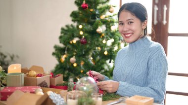 Mutlu kazaklı genç Asyalı kadın Noel hediyesini kurdele ile bağlayıp böğürtlenlerle süslerken Noel bayramı ve kış mevsimlerini evde kutlamak için hediyeler hazırlıyor..