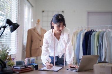 Boynuna mezuralar takan Asyalı genç tüccar kadınlar ve internet üzerinden siparişleri kontrol ediyorlar. İç işlerindeki online alışveriş işlerinde çalışırken not alıyorlar..