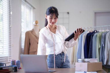 Genç Asyalı tüccar kadınlar online siparişleri ve müşteri bilgilerini kontrol etmek için dizüstü bilgisayarda veri yazarken tablete not alıyor ve merkez ofisteki çevrimiçi alışveriş işleri hakkında çalışıyor..