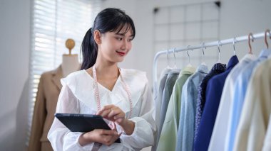 Genç Asyalı tüccar kadınlar mağazadaki stok giysi ürünlerini kontrol ederken ve dijital tablet hakkında çevrimiçi sipariş bilgileri alırken aynı zamanda ev ofisindeki çevrimiçi alışveriş işleri hakkında çalışmaktadırlar..