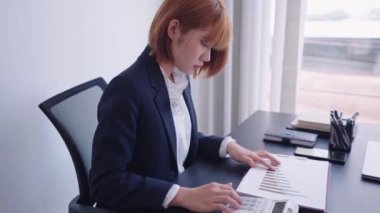 Profesyonel olarak giyinmiş kendine güvenen Asyalı bir iş kadını, üç aylık şirket performansını çalışma alanında özenle hesaplıyor. Kendini işine adadı ve görevlerine odaklandı.