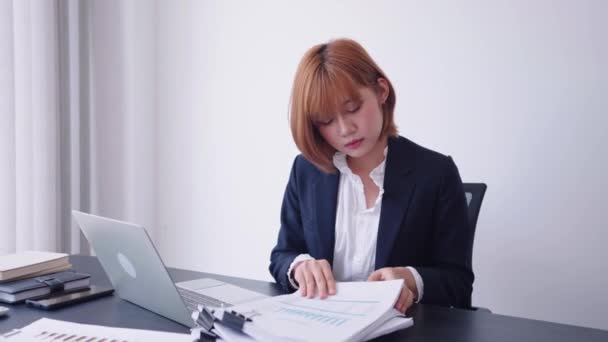 一位自信的亚洲女商人 坚定不移地在堆积如山的文件中搜寻着自己的工作文件 准备在她专用的工作空间里用她的笔记本电脑集中工作 — 图库视频影像