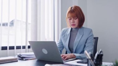 Enerjik bir Asyalı iş kadını, telefonda coşkuyla konuşurken aynı anda bilgisayarında çalışıyor, hareketli ve hareketli bir tavır sergiliyor. Yüksek kalite 4k görüntü