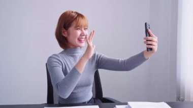 Zeki telefonuyla video görüşmesi yapan kendine güvenen Asyalı bir iş kadını geçici çalışma masasından ayrılıp arkadaşlarıyla bağlantı kurmaktan zevk alıyor.