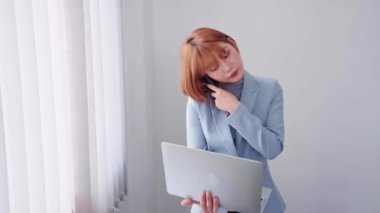 Enerjik bir Asyalı iş kadını, telefonda coşkuyla konuşurken aynı anda bilgisayarında çalışıyor, hareketli ve hareketli bir tavır sergiliyor. Yüksek kalite 4k görüntü