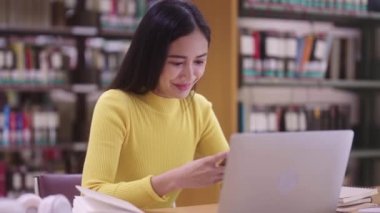 Asyalı güzel bir bayan öğrenci masada oturuyor ve cep telefonu kullanıyor ya da sosyal medyada mesajlaşıyor ya da kütüphanede ödev yaparken ya da kitap okurken şarkı dinliyor. Yüksek kalite 4k görüntü